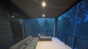 A covered outdoor seating area with a wooden deck, a sofa, and a bench.