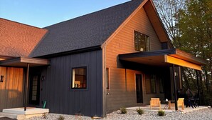 A modern house with a dark exterior, a sloped roof, and a covered porch area with outdoor seating.