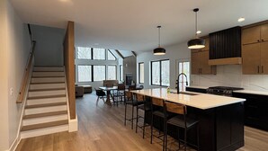 A modern kitchen with a central island, wooden flooring, and a staircase leading to another level.