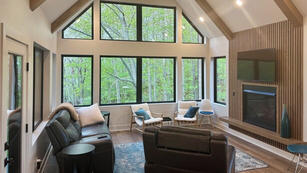 A spacious living room with a fireplace, large windows, and a high ceiling.