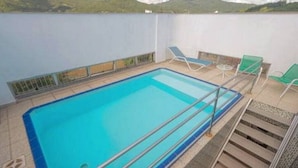 Piscina en la azotea con agua cristalina y azul, rodeada por un muro blanco y una barandilla de metal.