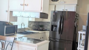 A compact kitchen with white cabinets, a stainless steel refrigerator, a microwave, and a small island with a sink. - This property is shared with the Host. On the corner in a welcoming neighborhood (Lima)