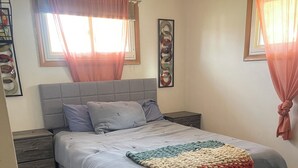 Un dormitorio con una cama, mesitas de noche, una alfombra y cortinas.