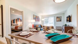 A modern dining area with a large table set for six, a sofa in the background, and artwork on the walls.