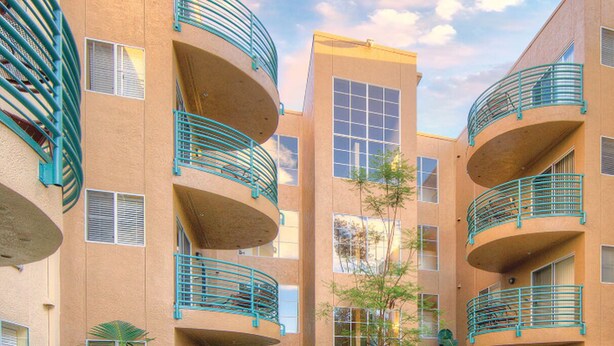 A multi-story building with balconies, large windows, and a central courtyard with trees.