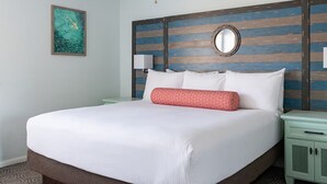 A neatly made bed with white linens and a red pillow, a round mirror on the headboard, and a small nightstand with a lamp.