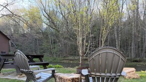 A picnic table with two Adirondack chairs, a wooden stump, and a river in the background.