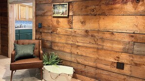 A room with a wooden wall, a brown leather chair, a green cushion, and a plant in a white pot.