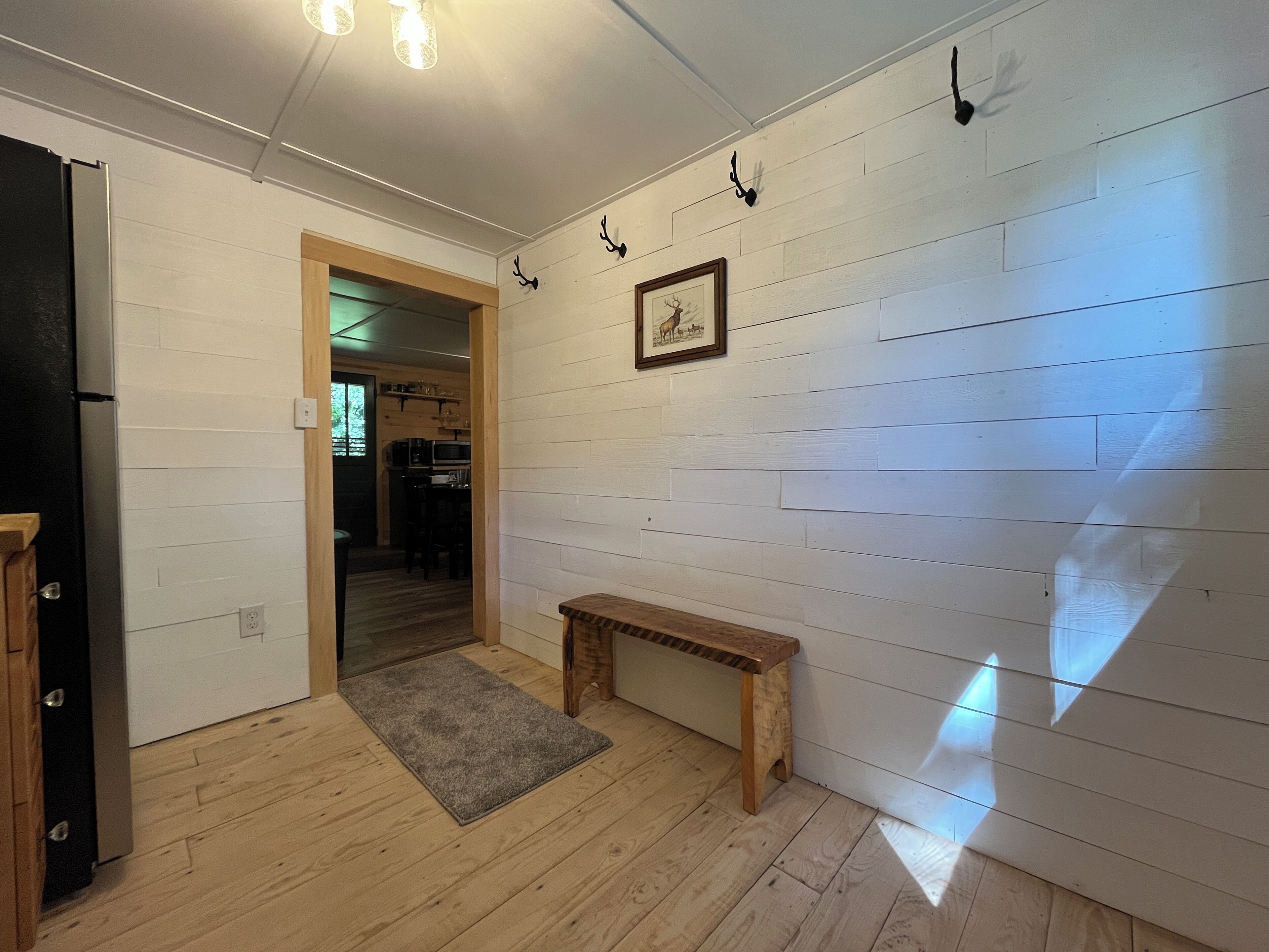 Une pièce aux murs en bois peints en blanc, avec un banc en bois, un tapis et un tableau encadré.