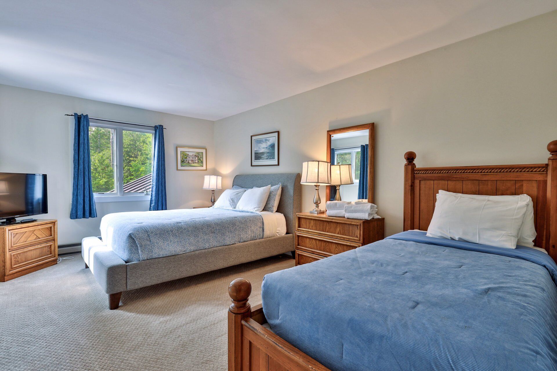 A hotel room with two beds, a television, a dresser, and a window with curtains.