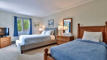 A hotel room with two beds, a television, a dresser, and a window with curtains.