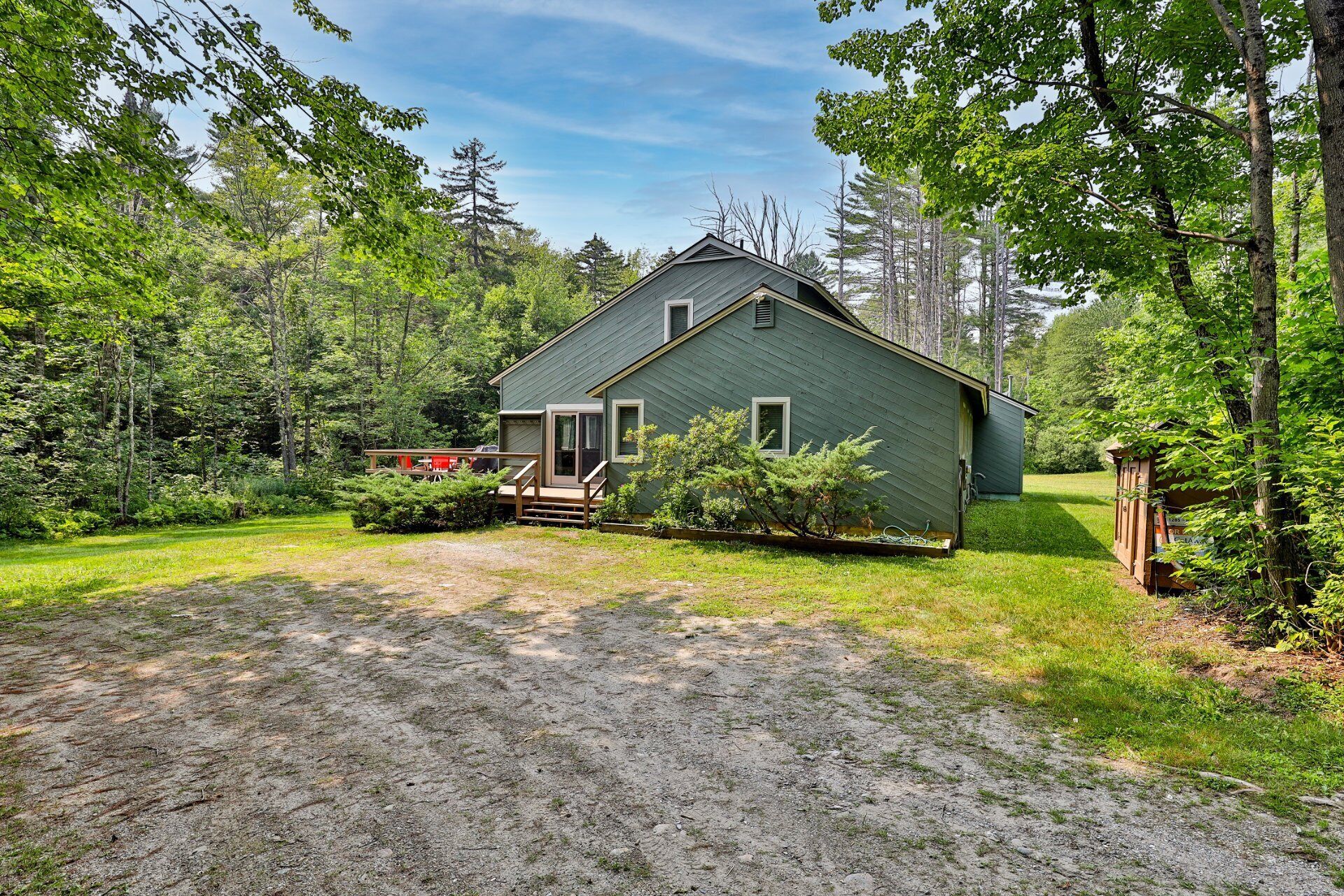 A rustic cabin with a gravel driveway, surrounded by dense forest.