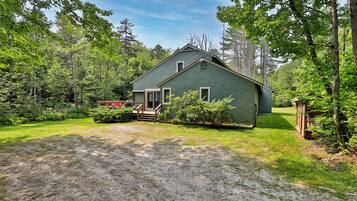 A rustic cabin with a gravel driveway, surrounded by dense forest.