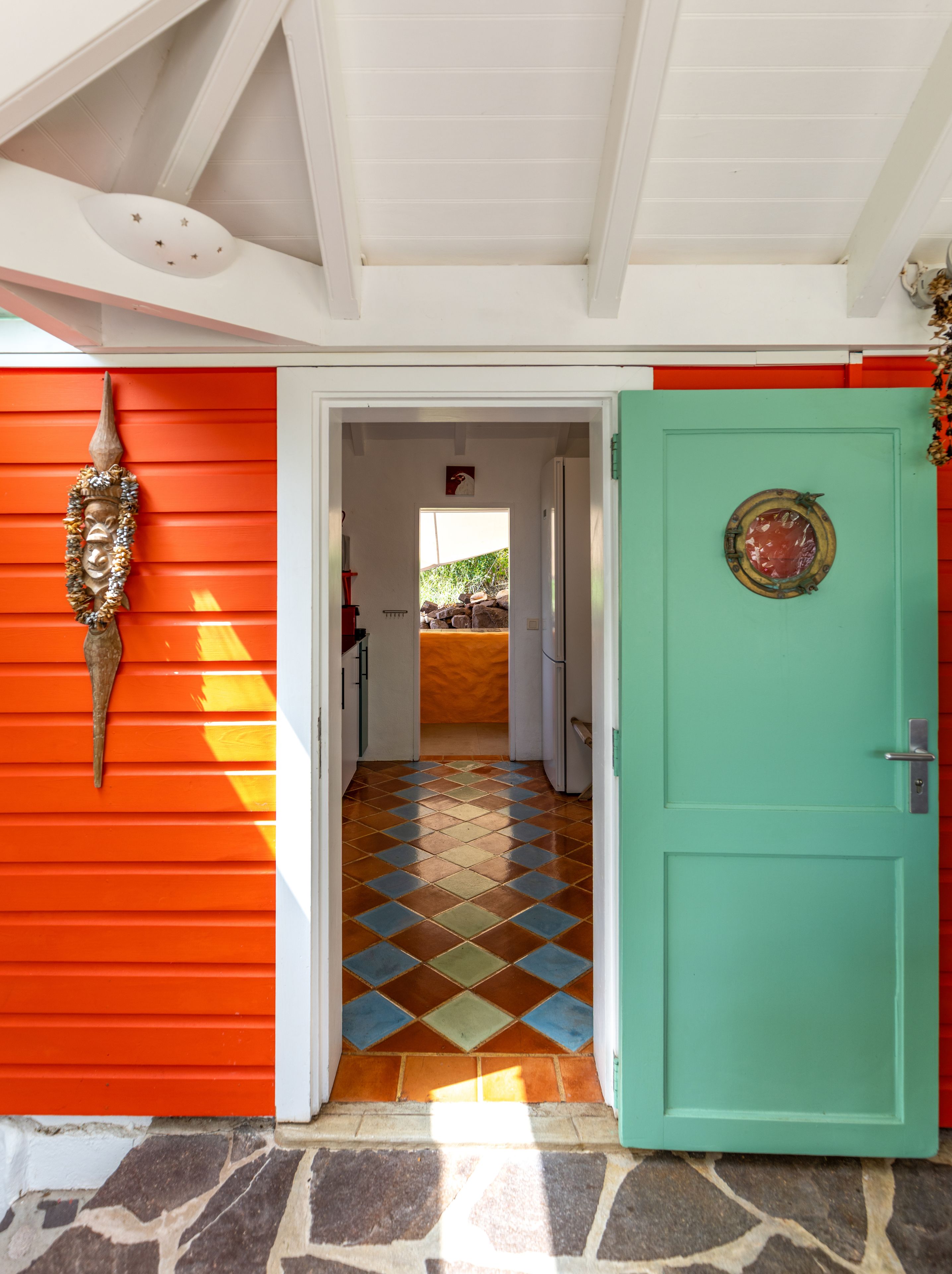 A hallway with a tiled floor, a green door, and a red wall with a decorative mask.