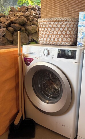 A front-loading washing machine with a control panel, a mop, and a basket on top.