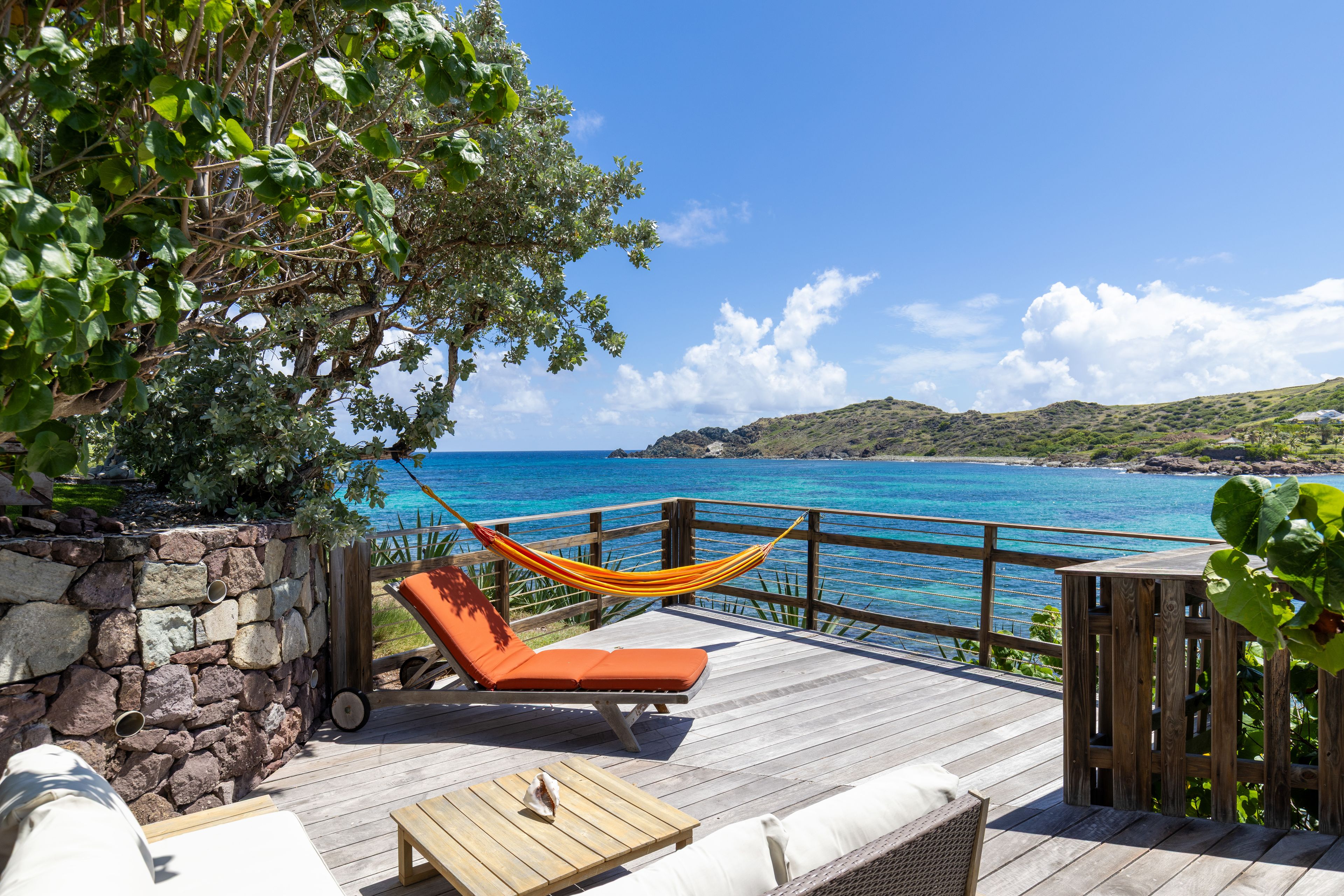 A wooden deck with a hammock, lounge chairs, and a view of the ocean.