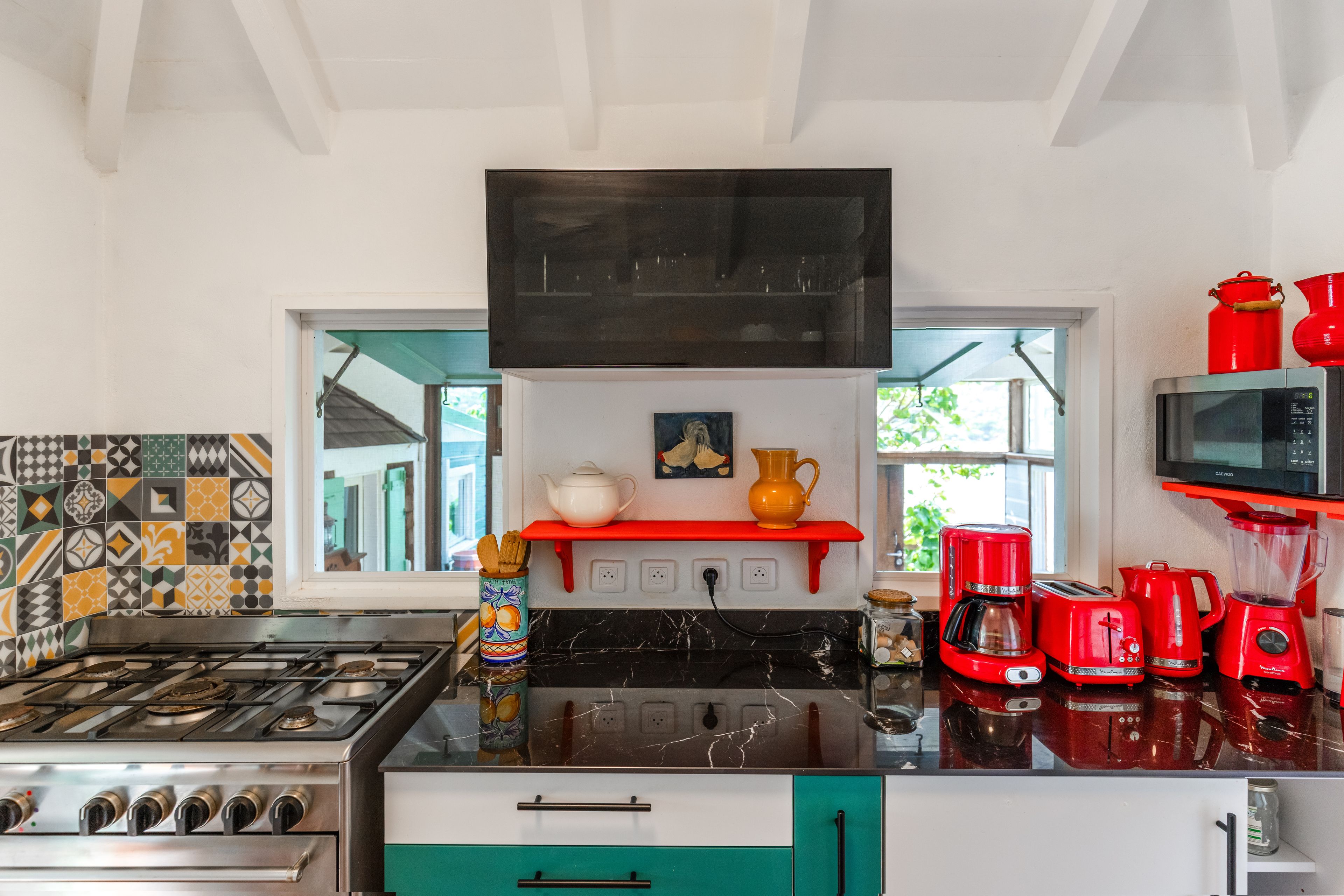 A kitchen with a gas stove, a microwave, red appliances, and a patterned backsplash.