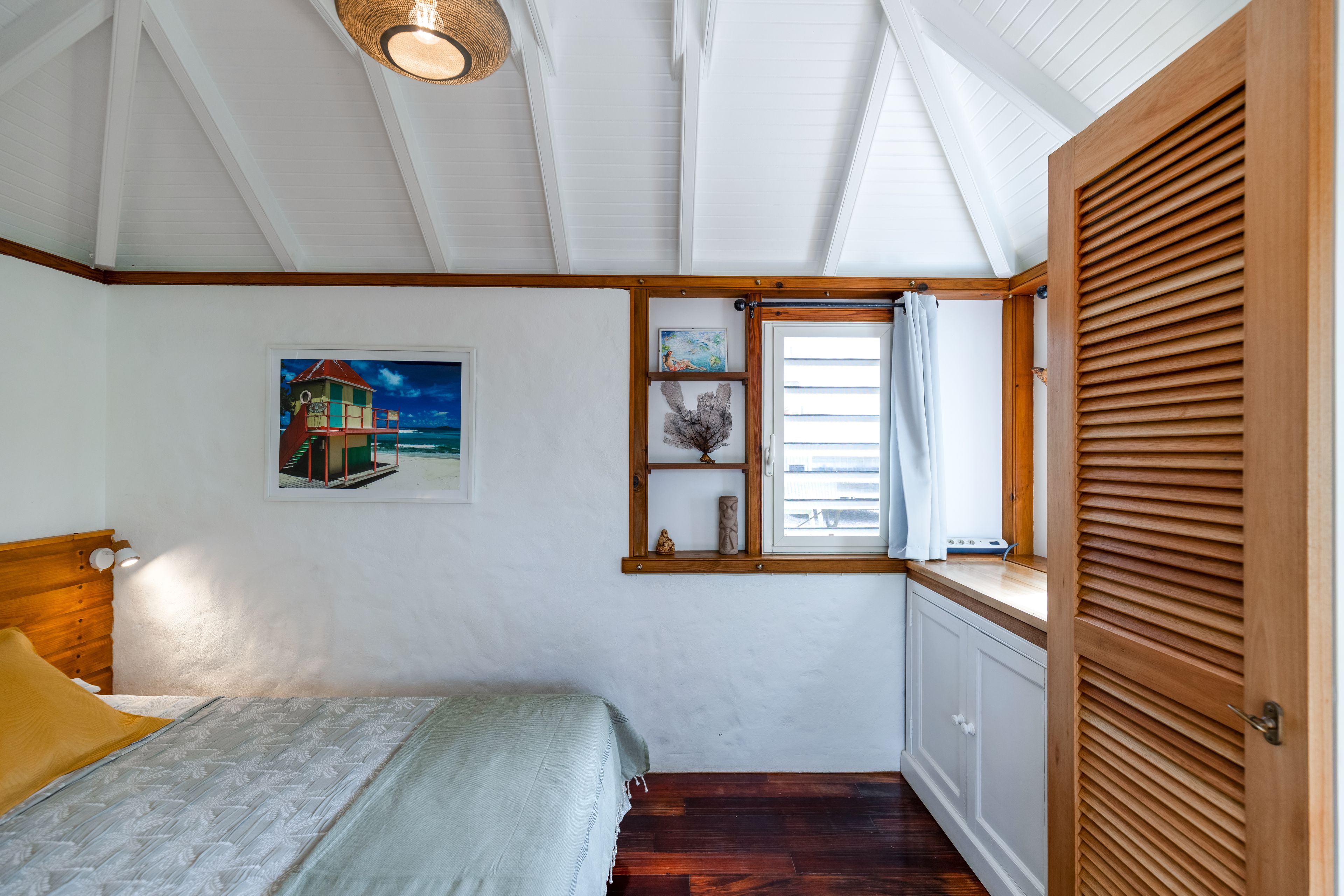A bedroom with a bed, a window with a view, a painting on the wall, and a wooden door.