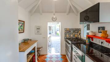 A kitchen with a tiled floor, a stove, a sink, and a wooden table with a bowl.