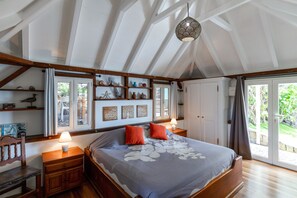 A bedroom with a large bed, wooden headboard, bedside tables, a hanging light fixture, and a view through the window.