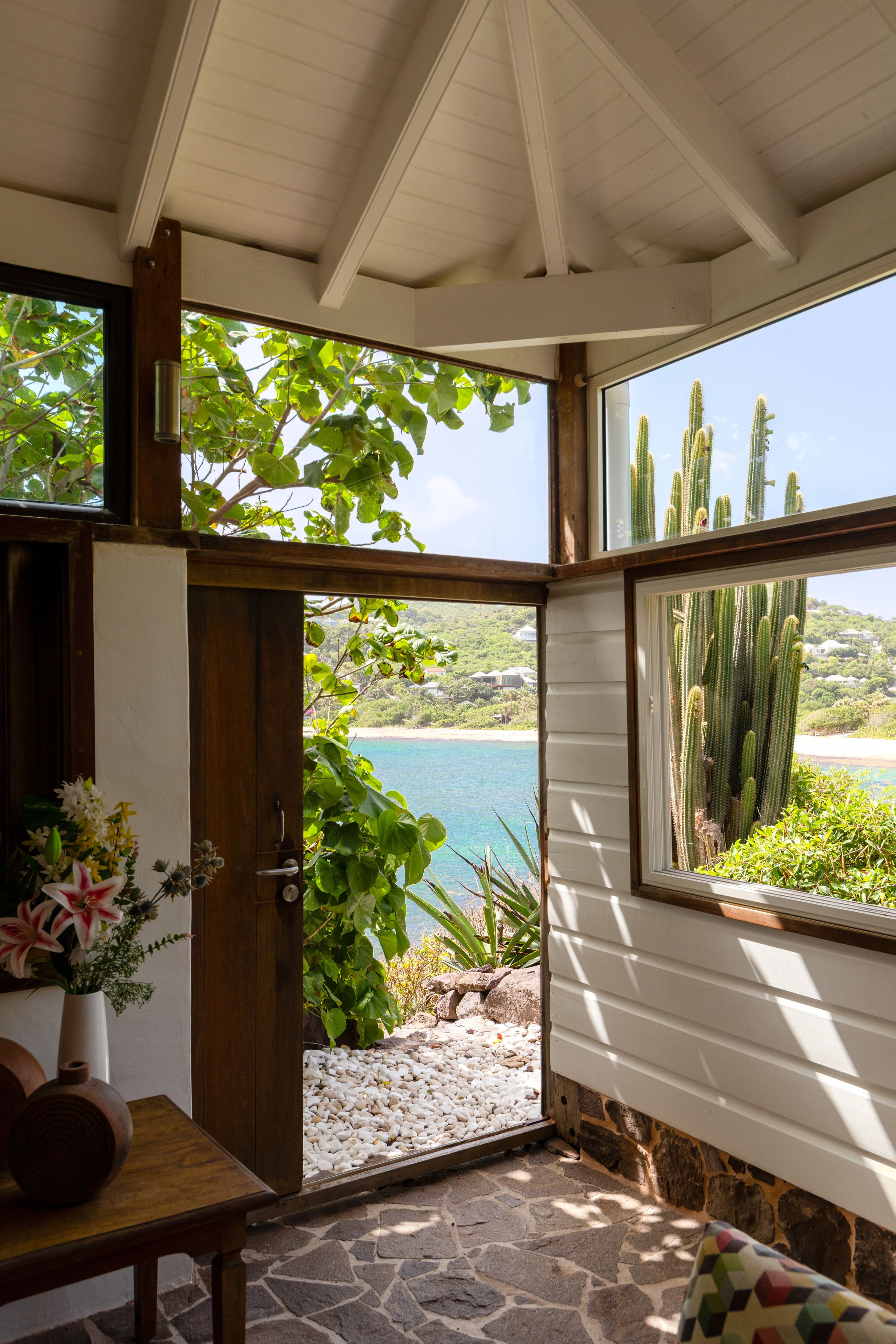 A room with a view of a beach and cacti through a large window.