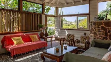 A sunlit room with a red sofa, patterned armchairs, and a stone wall.