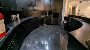 Une cuisine moderne avec des meubles de couleur sombre, un comptoir incurvé et une hotte de cuisinière en acier inoxydable.