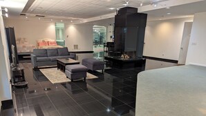 Un salon moderne avec un sol carrelé noir, des canapés gris et une cheminée.
