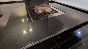 Un intérieur moderne avec un élégant comptoir noir, un barbecue intégré et une vue sur une forêt, visible à travers de grandes fenêtres.