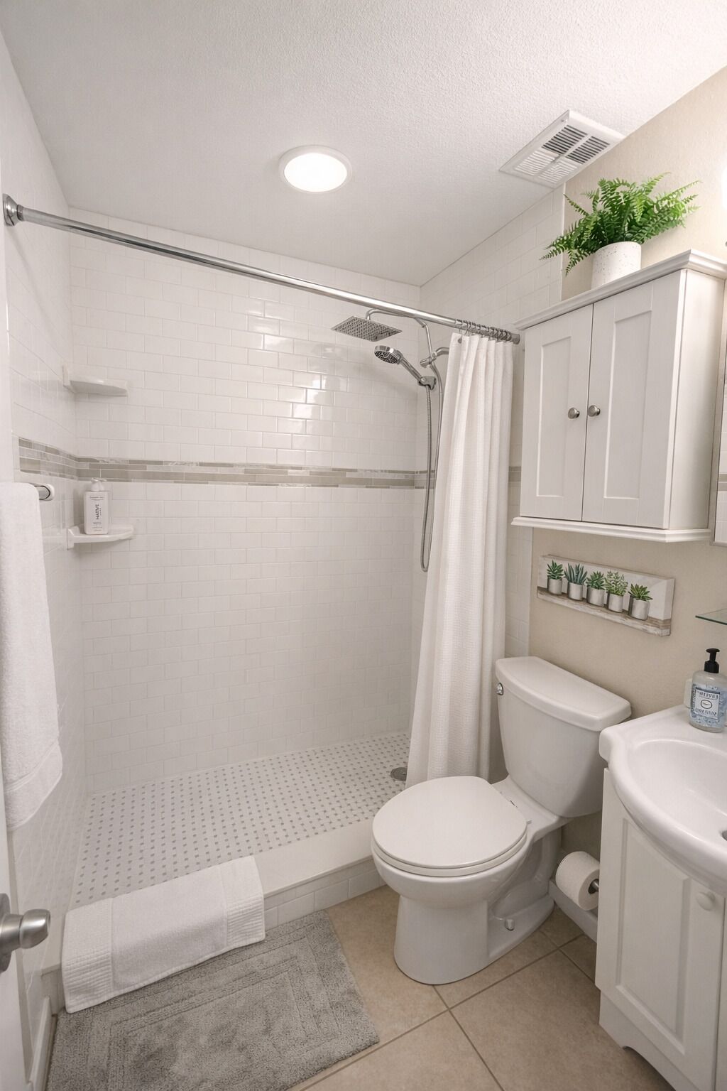 Et badeværelse med bruser, toilet, vask og en lille plante på væggen.