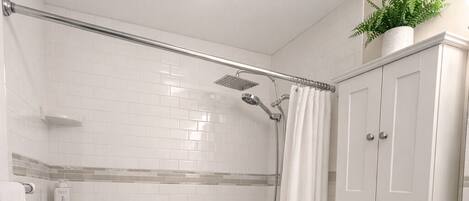 Et badeværelse med bruser, toilet, vask og en lille plante på væggen.