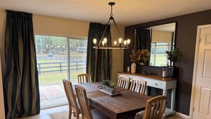 A dining area with a wooden table, chairs, a chandelier, a mirror, and a view of the outdoors. - Steps to WEC - Geneva Maison @ Swiss Stables on rare 20 acre estate (Ocala)