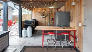 A compact kitchen with a wooden table, bar stools, a refrigerator, and a gas grill. - Cozy Bungalow W/ Lake Access - Near Mt. Rainier (Eatonville)