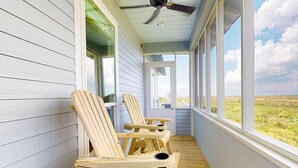 Une véranda couverte avec des chaises en bois et un ventilateur de plafond.