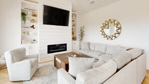 Un salon moderne avec un canapé d’angle, un téléviseur à écran plat, une cheminée et des étagères intégrées.