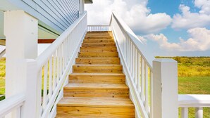 Un escalier en bois, doté de rampes blanches, mène à un bâtiment à la façade bleue.