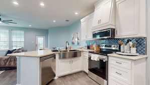 A modern kitchen with white cabinets, stainless steel appliances, and a blue backsplash. - Retreat | Gulf Views | Large Deck | Group Ready (Freeport)