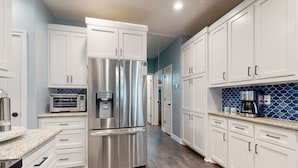 A modern kitchen with white cabinets, stainless steel appliances, and a blue backsplash. - Retreat | Gulf Views | Large Deck | Group Ready (Freeport)