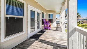 A covered porch with a wooden deck, a purple chair, and a door with a screen. - Retreat | Steps to Beach | Dog Haven | Sleeps 12 (Crystal Beach)