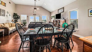 A dining area with a table set for four, surrounded by black chairs, in a room with wooden flooring and a ceiling fan. - Retreat | Steps to Beach | Dog Haven | Sleeps 12 (Crystal Beach)