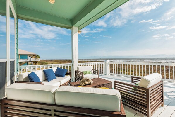 A covered outdoor seating area with a view of the ocean, featuring a sofa, chairs, and a table.