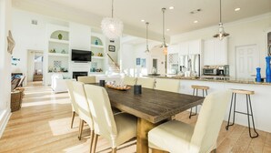 A spacious kitchen with a wooden dining table, white chairs, and pendant lighting.