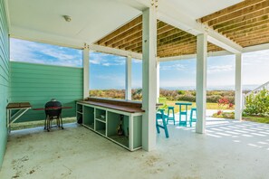 En udendørs overdækket terrasse med grill, siddepladser og udsigt over landskabet.