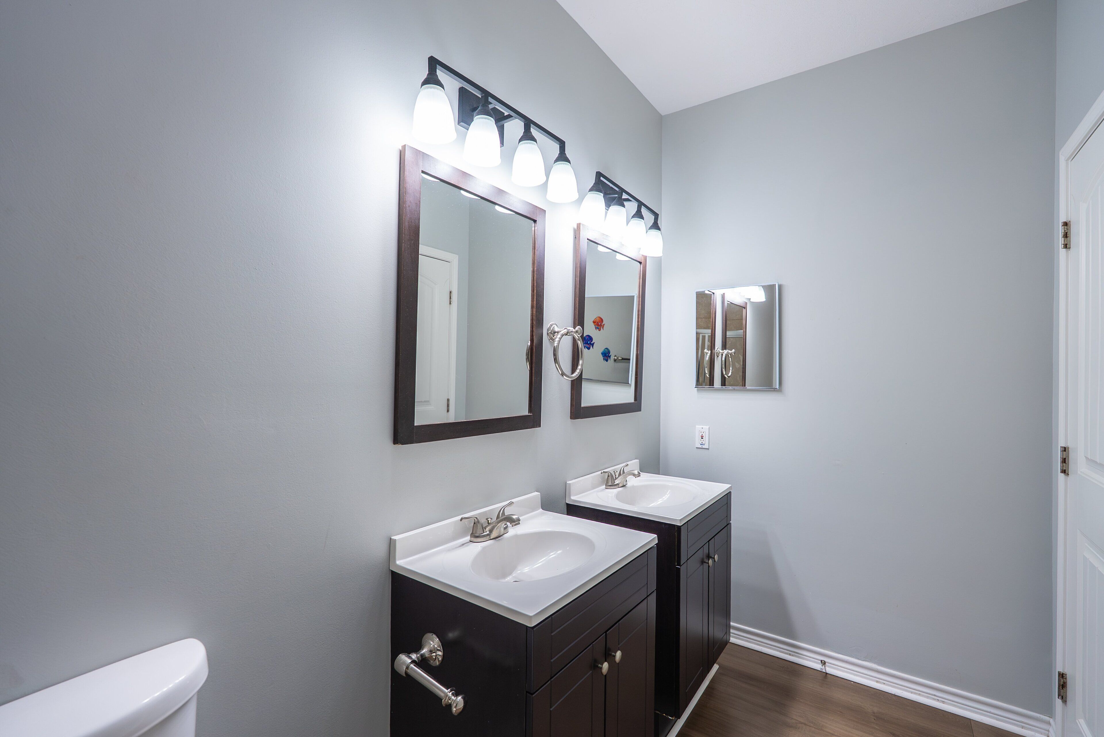 A bathroom with two sinks, a toilet, and a mirror with lights.