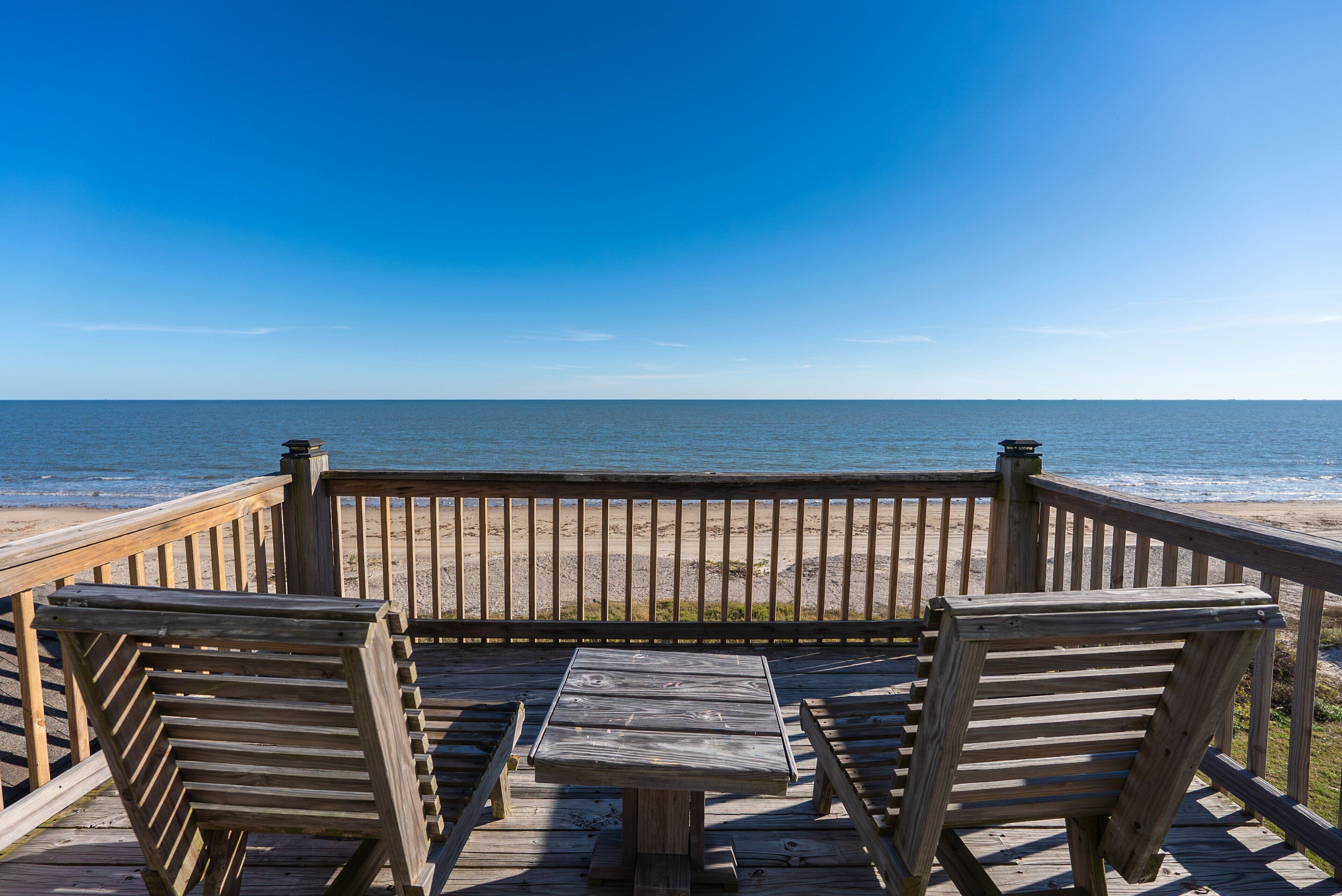 A wooden deck with a table and chairs overlooking a beach.