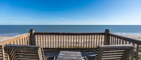 A wooden deck with a table and chairs overlooking a beach.