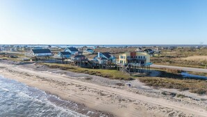 Une zone côtière avec des maisons sur pilotis, une plage de sable et une route menant à la mer.