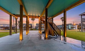 A covered outdoor area with a concrete floor, wooden columns, and a staircase leading to an upper level. - Amazing | Gulf Views | Large Deck | Family Fun (Freeport)