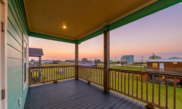 A wooden deck with a railing, a porch, and a view of houses and a body of water. - Amazing | Gulf Views | Large Deck | Family Fun (Freeport)