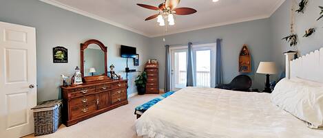 A bedroom with a bed, dresser, ceiling fan, and a window with curtains.